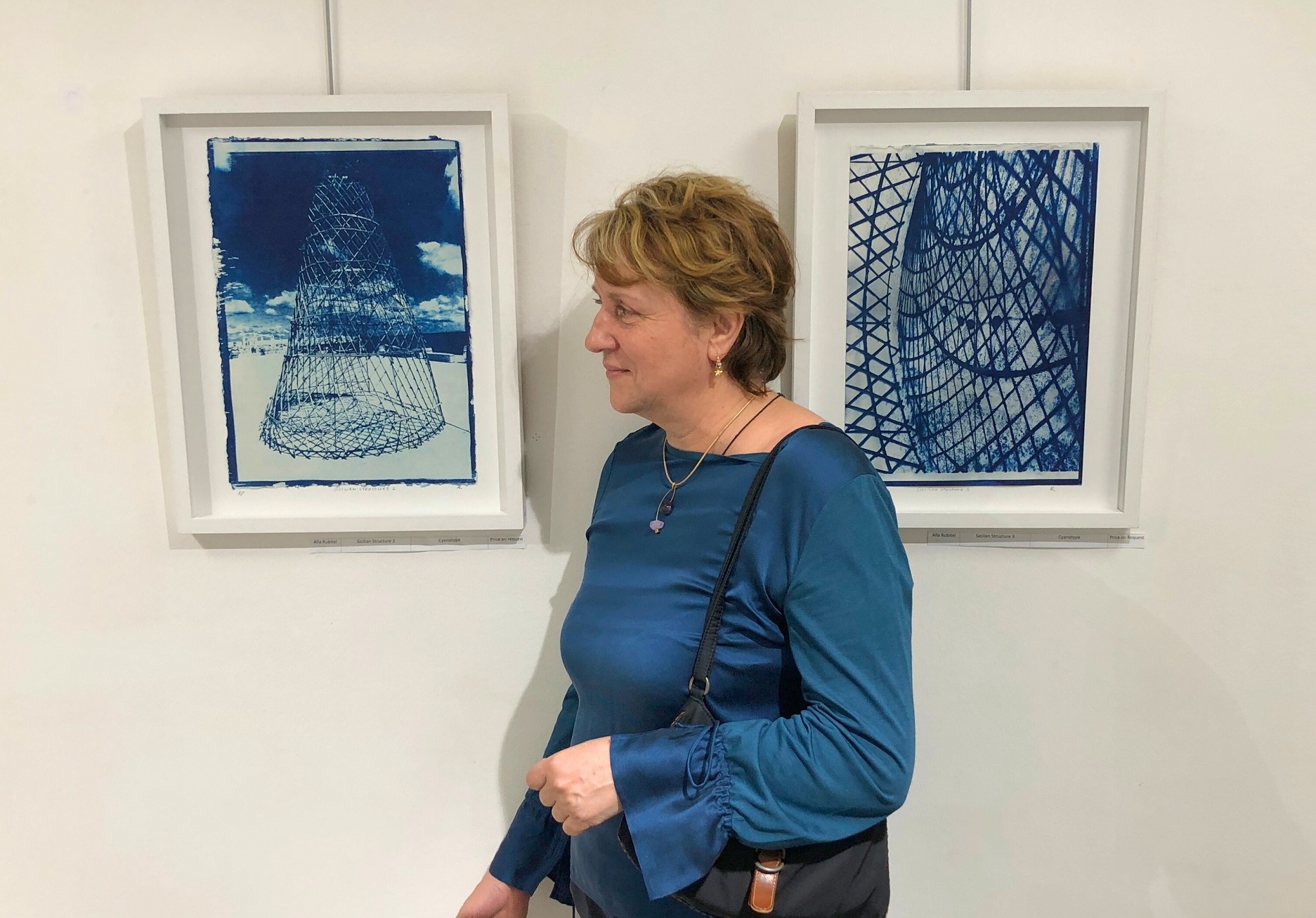 Woman wearing a blue blouse and a handbag standing with her profile to the camera in front of a wall with two blue-tinted artworks