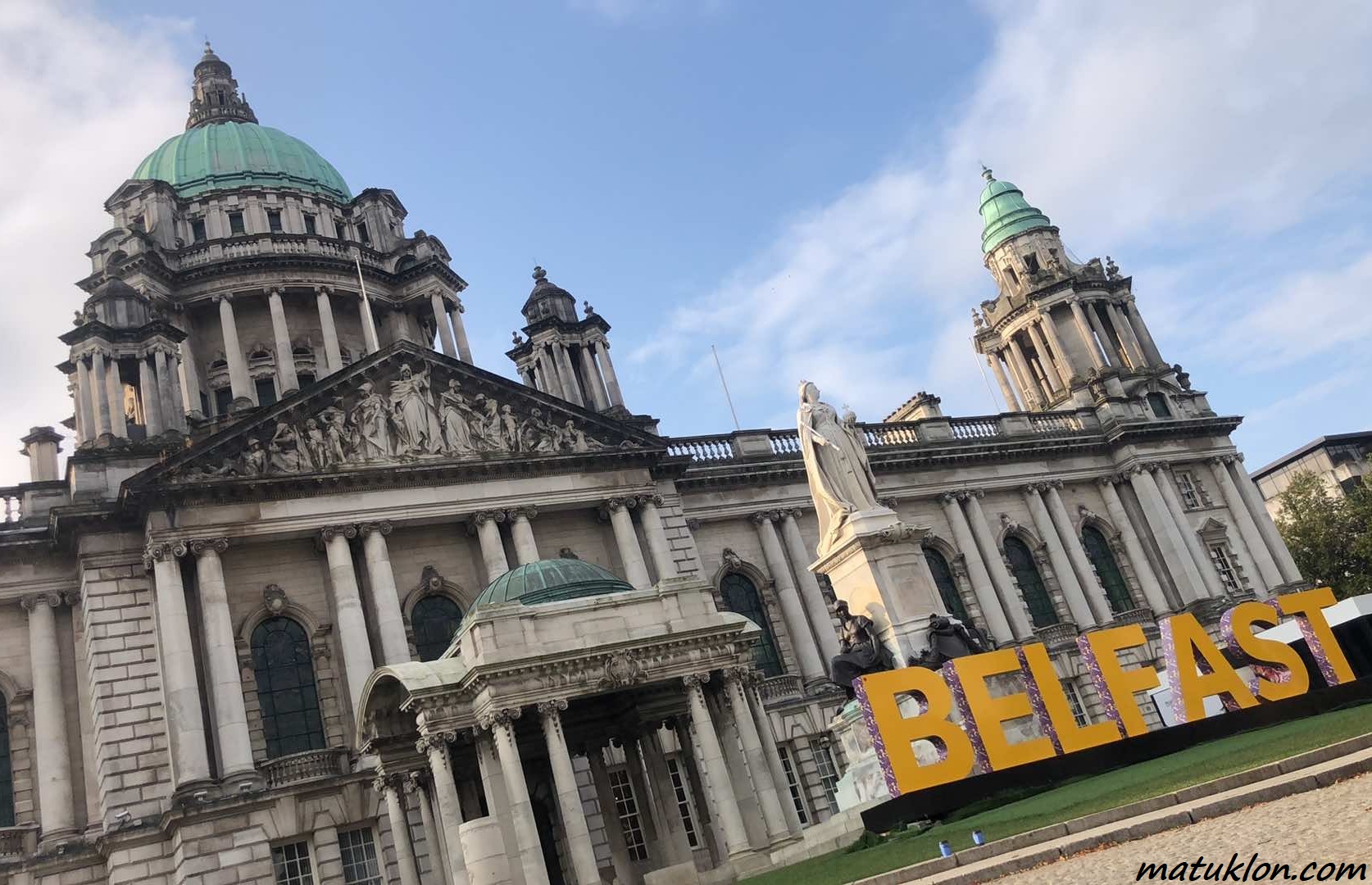 Neo-Baroque building, with columns and a dome, and huge yellow letters spelling BELFAST in front of it