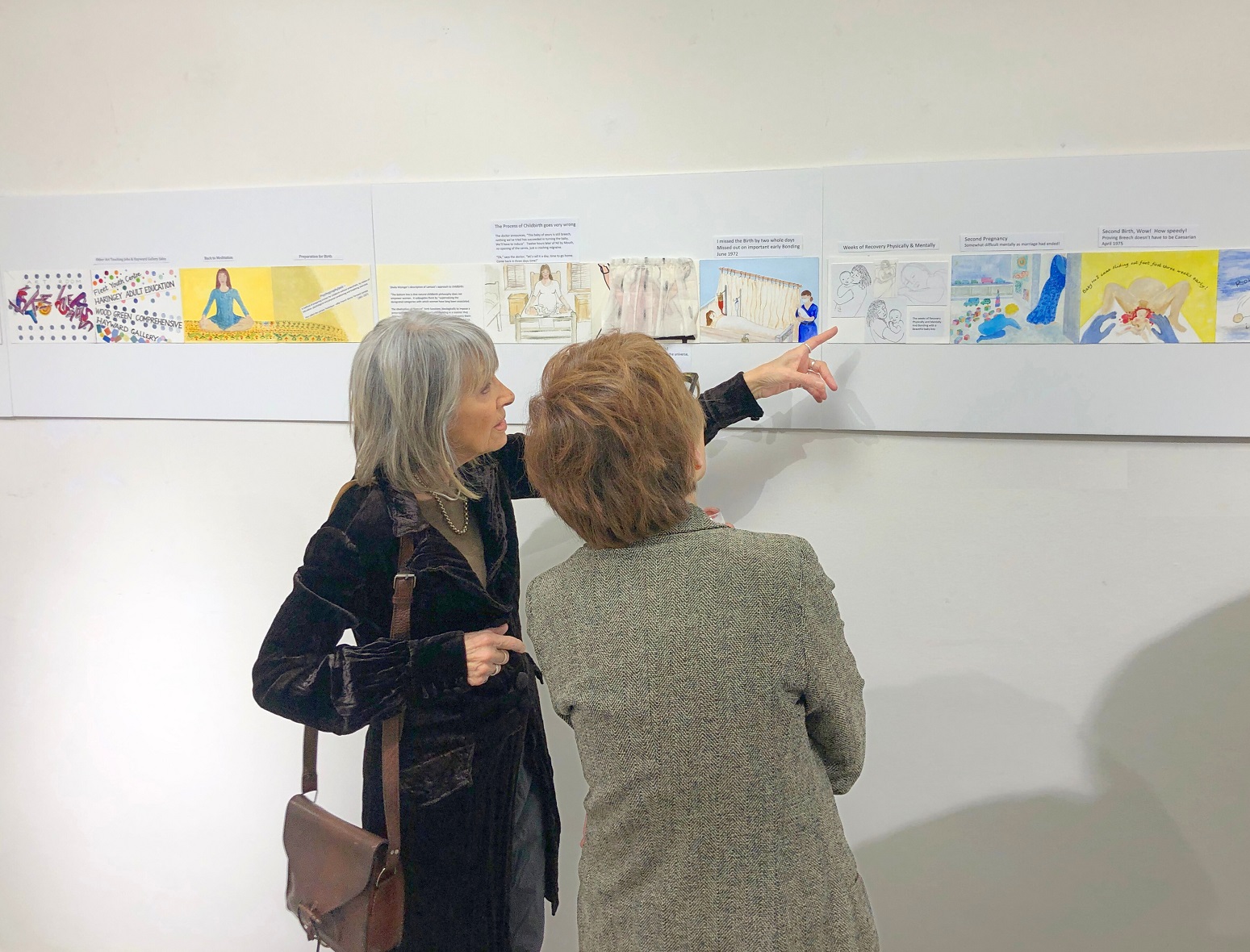 Two women looking at artworks on the wall; one of the women is pointing at an artwork