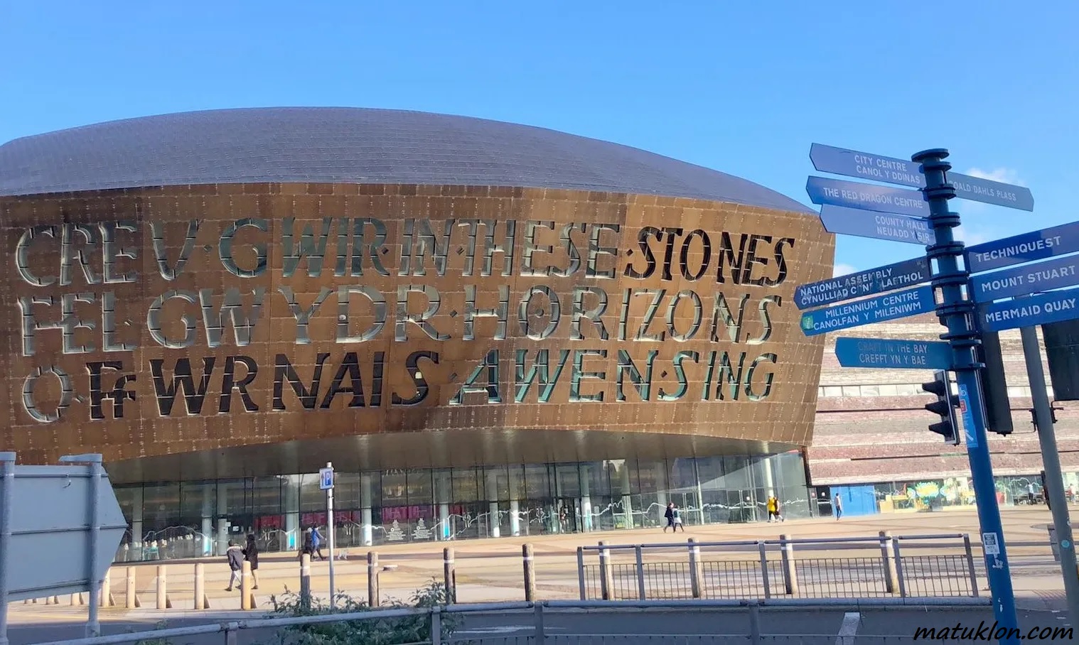 Round brown building against blue sky, with fingerpost on the right